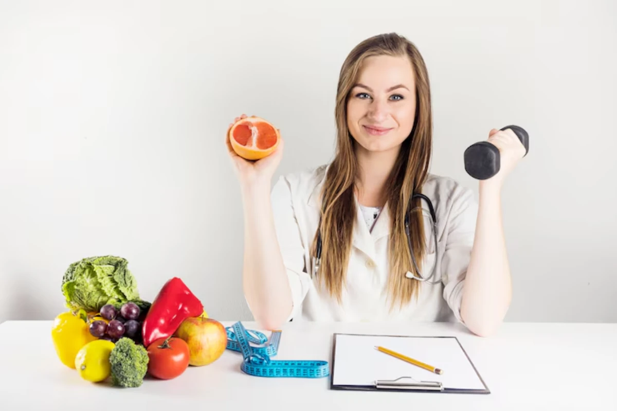 A healthcare professional holds a grapefruit in one hand and a dumbbell in the other, surrounded by fresh fruits and vegetables.