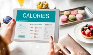 A hand holding a tablet displaying calorie information and activities to burn 70 calories, with desserts in the background.