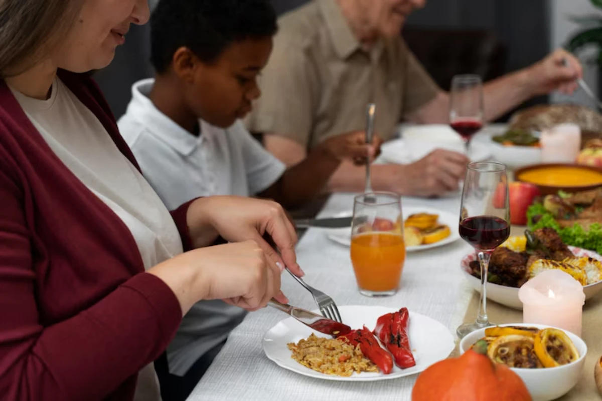 A dining table filled with various dishes; a person cuts into a plate of rice and peppers, surrounded by family enjoying a meal.