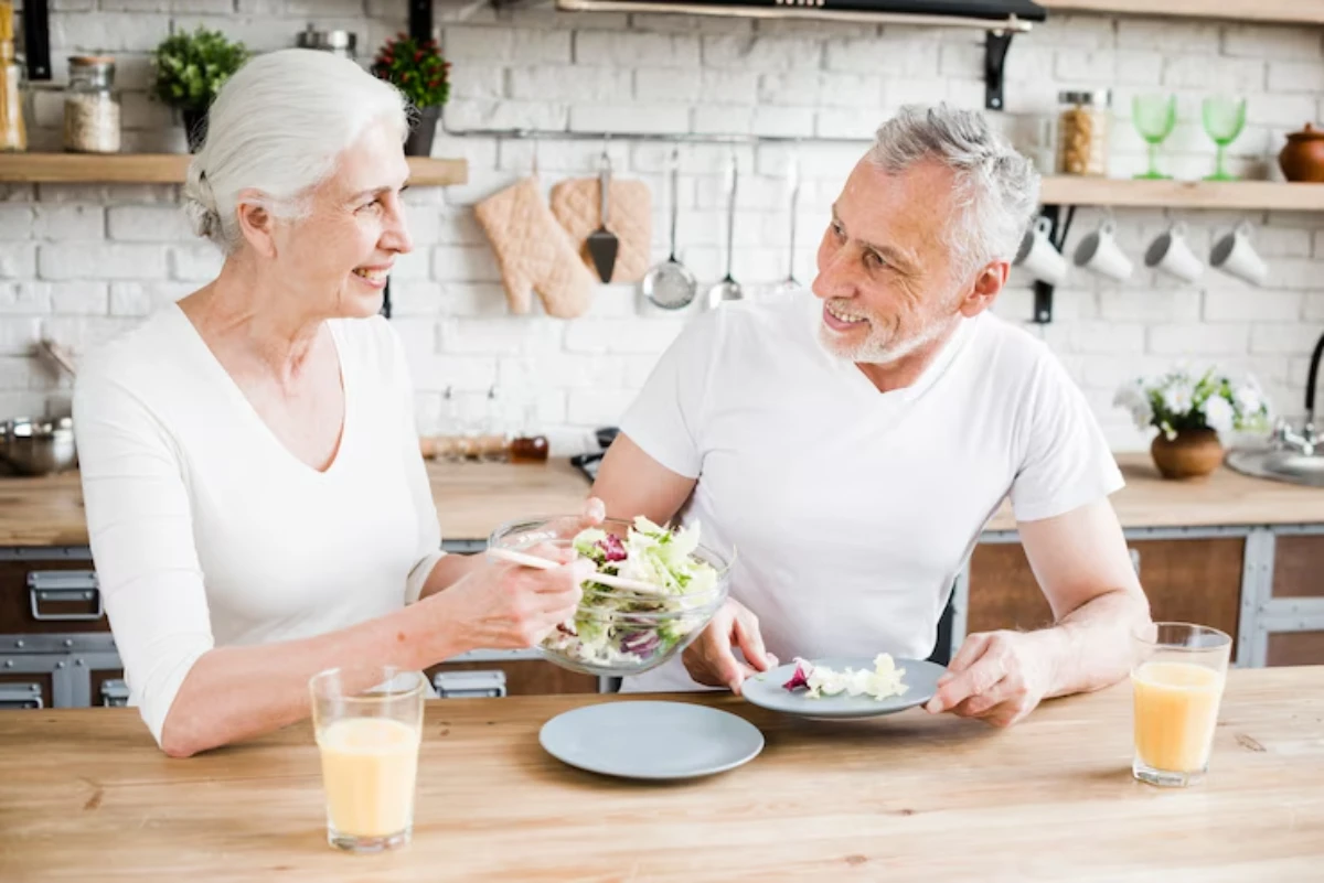 A woman serves a fresh salad to a man at a rustic kitchen table, with glasses of orange juice nearby. Bright and inviting atmosphere.
