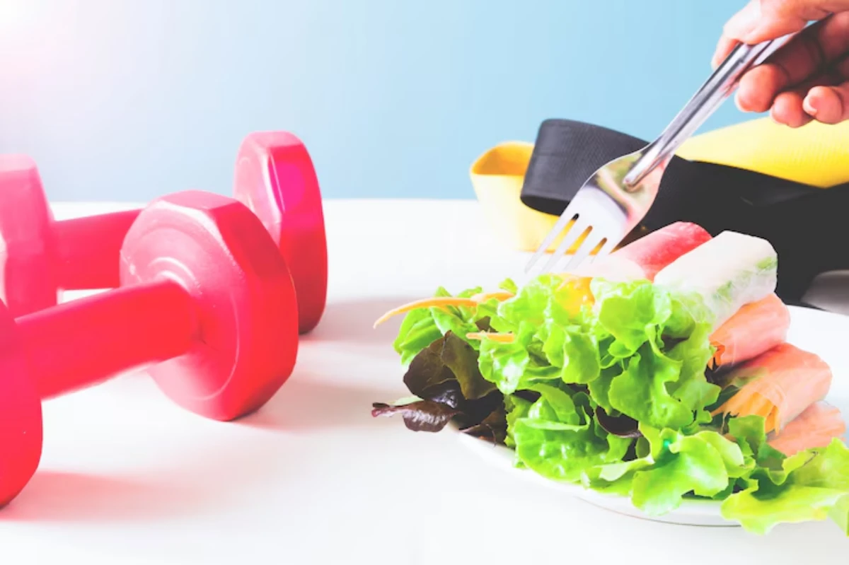 A hand holding a fork above a fresh salad with lettuce and colorful vegetables, next to red dumbbells and workout bands.