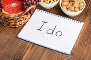 A notebook with I do written on it, surrounded by a basket of grapes, grapefruit slices, and bowls of snacks on a wooden table.