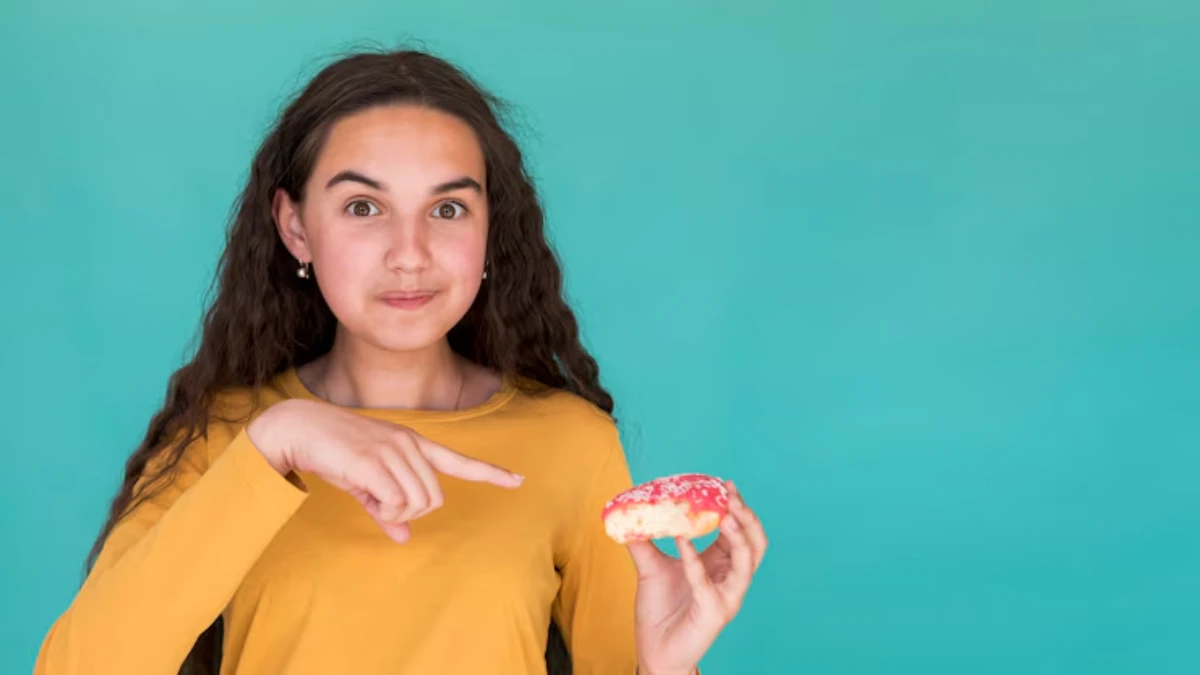 A person in a yellow shirt points at a donut with pink icing and sprinkles, set against a bright teal background.