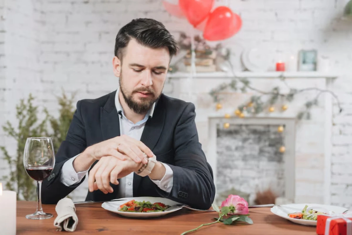 A man in a suit sits at a beautifully set table with candles, wine, and a plate of salad, surrounded by a romantic ambiance.