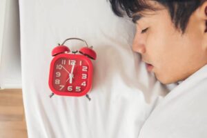 A red alarm clock is resting on a white bedsheet, indicating the time and adding a pop of color to the serene bedroom setting.