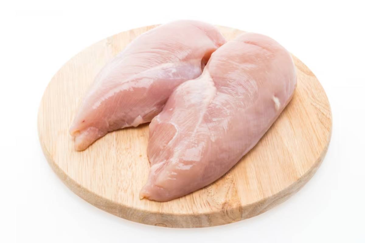 Two raw chicken breasts resting on a circular wooden cutting board, ready for preparation or cooking.